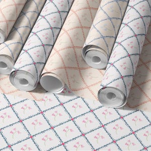 May include: Several rolls of wallpaper with a repeating pattern of pink bell flowers within a diamond grid. The background colors vary from white to beige. The edges of the diamonds are outlined in blue and pink.