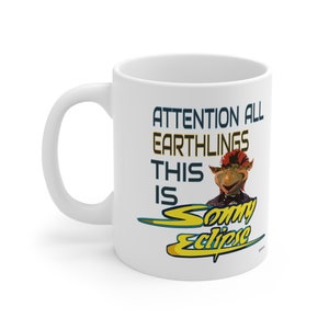 May include: White ceramic mug with a colorful illustration of a character with red hair and a blue shirt. The text on the mug reads "Attention all Earthlings This is Sonny Eclipse".