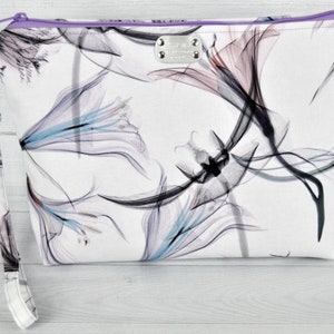 Large pouch in abstract cotton print with wrist strap attached on light background. White, black turquoise, plum and lavender flowers. Lavender zipper.