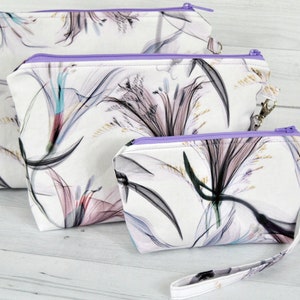 3 piece pouch set in abstract cotton fabric. White, black, turquoise, plum and lavender. Detachable wrist straps. Sitting on a light background.