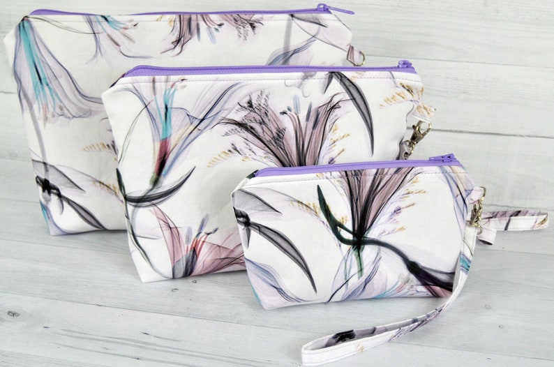 3 piece pouch set in abstract cotton fabric. White, black, turquoise, plum and lavender. Detachable wrist straps. Sitting on a light background.