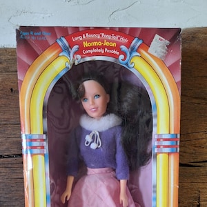 May include: A vintage-style doll box featuring a girl doll with long brown hair, wearing a purple sweater and a pink skirt. The box has a jukebox design with the words "Bobby Sox" and "The Fun & Fabulous Fifties are Back!" printed on it.