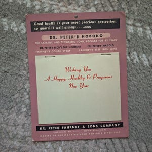 May include: A vintage pink promotional card from Dr. Peter Fahrney & Sons Company featuring black text and a cream-colored insert. The text reads: Good health is your most precious possession, Dr. Peter's Hoboko, and Wishing You A Happy, Healthy & Prosperous New Year.