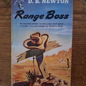 May include: Vintage paperback book cover for "Range Boss" by D.B. Newton. The cover features a cowboy hat on a wooden cross with a desert landscape backdrop. The title is in bold, with text below. "Pocket Book" is at the top.
