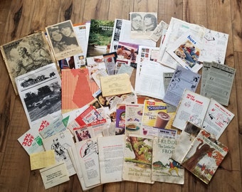 May include: A collection of vintage paper ephemera, including magazines, newspapers, and advertisements. The papers are scattered on a wooden surface and feature a variety of images and text, including a car, a tree, and a frog. The papers are in various states of wear and tear, giving them a vintage look.