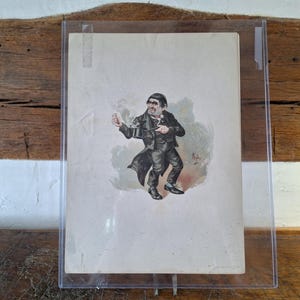 Può includere: Una stampa antica incorniciata di un uomo in abito e cappotto neri, con in mano una piccola pentola e un bicchiere. La stampa ha uno stile colorato e caricaturale. La cornice è in plastica trasparente e lo sfondo è una superficie di legno.
