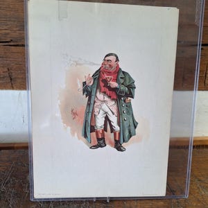Può includere: Una stampa di caricatura vintage incorniciata. L'illustrazione raffigura un uomo con un lungo cappotto verde, sciarpa rossa e pantaloni bianchi, che fuma la pipa. La stampa è protetta da una custodia di plastica trasparente, su una superficie di legno.