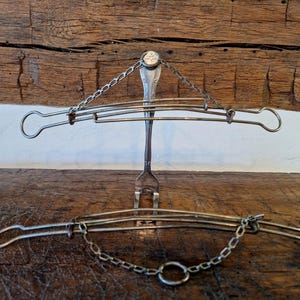 May include: A silver fork with a chain attached to the top, forming a hanging structure. The fork is bent into a curved shape, and the chain is connected to two metal rings on either side. The structure is hanging from a wooden surface.