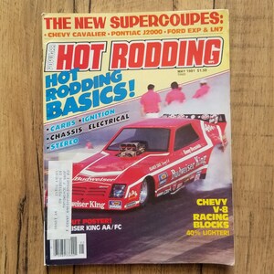 以下が含まれることがあります： 「Budweiser King」と書いてある赤、白、青のドラッグレースカー。車はタイヤから煙が出ているトラックの上にある。雑誌の表紙は、1981年5月号の「Hot Rodding」誌。表紙のテキストは「新しいスーパークーペ：シボレー・キャバリエ、ポンティアック・J2000、フォード・EXP & LN7」です。