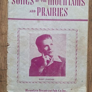 Peut inclure: Une couverture de livre de musique vintage avec le titre "Songs of the Mountains and Prairies" en lettres roses. Une photo en noir et blanc d'un homme avec une teinte rose est présentée sur la couverture. L'homme porte une chemise à col et regarde la caméra. Le texte "Buddy Starcher" est sous la photo. Le texte "Mountain Broadcast Pub. Co. Inc., 45 Astor Place, New York 3, N. Y." est en bas de la couverture.