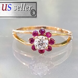May include: A gold ring with a single round diamond surrounded by a cluster of small red gemstones. The ring has a delicate, open design.