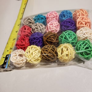 May include: A clear plastic bag filled with colorful woven balls. The balls are in various colors, including pink, blue, green, and yellow. A yellow tape measure is in the upper left corner, showing measurements in inches.