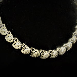 May include: Silver-toned necklace with a leaf and pearl design. The necklace features a series of interconnected leaf-shaped links, each with a small, round pearl in the center. The leaves are detailed with intricate veining.