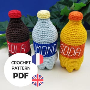 以下が含まれることがあります： 3本のクロシェ編みソーダボトルのクロシェパターンPDF。ボトルは茶色、青、黄色で、「コーラ」、「レモネード」、「ソーダ」の文字が書かれています。