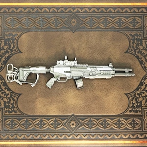 May include: A silver-colored metal keychain shaped like a rifle with a black handle and a red sight. The keychain is on a brown leather background with an ornate border.