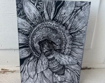 May include: Black and white illustration of a bee inside a sunflower. The bee is detailed with intricate patterns and the sunflower is drawn with a mandala-like design.