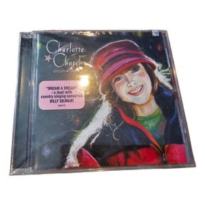 May include: A sealed CD case featuring the album "dream a dream" by Charlotte Church. The cover art depicts a smiling girl wearing a red and pink hat and coat. A pink sticker highlights the duet with Billy Gilman.