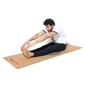 May include: A person stretches on a brown cork yoga mat with the text "Sakti Warrior" printed on it.