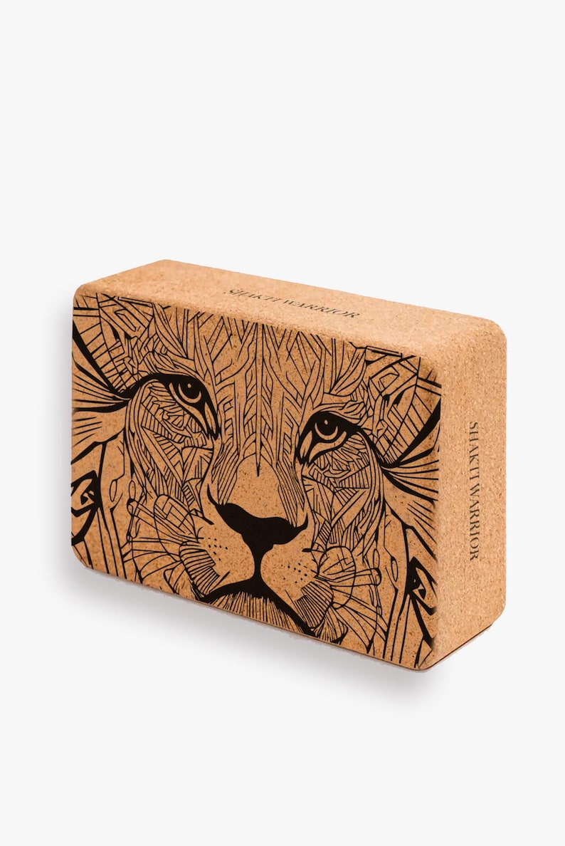 K&ouml;nnte beinhalten: Kork-Yoga-Block mit einer Schwarzwei&szlig;-Illustration eines L&ouml;wenkopfes. Der Block hat den Text "Shakti Warrior" auf der Seite.