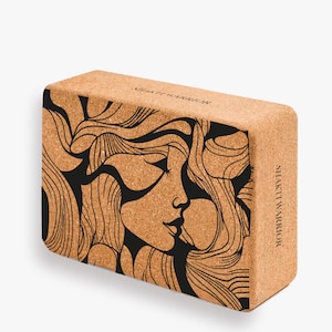 K&ouml;nnte beinhalten: Ein Kork-Yogablock mit einer schwarz-wei&szlig;en Illustration eines Frauenkopfes mit wallendem Haar. Der Text "Shakti Warrior" ist auf der Seite des Blocks aufgedruckt.