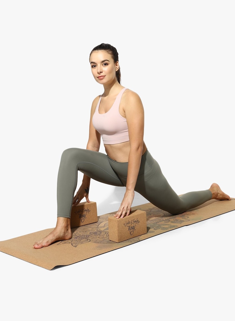 Puede incluir: Una mujer con un sujetador deportivo rosa y leggings verdes est&aacute; haciendo una pose de yoga en una esterilla de yoga de corcho con dos bloques de yoga de corcho. Los bloques tienen el texto "Soul & Body Magic" impreso en ellos.