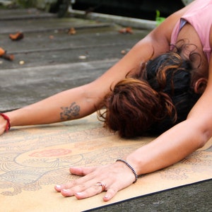 Puede incluir: Una persona practicando yoga en una esterilla con estampado. La persona lleva un top rosa y leggings morados. La esterilla es marr&oacute;n con un dise&ntilde;o de mandala colorido.