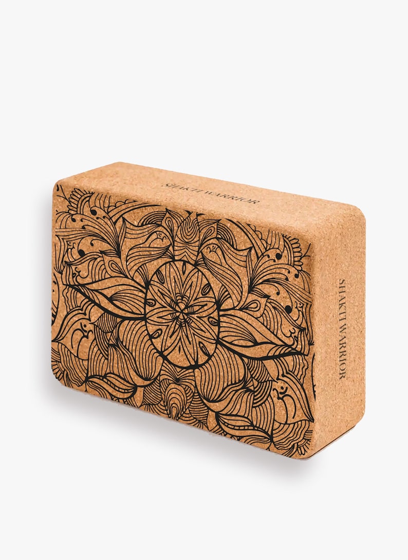 K&ouml;nnte beinhalten: Ein brauner Kork-Yogablock mit einem schwarzen Mandala-Design und dem Text "Shakti Warrior" auf der Seite.