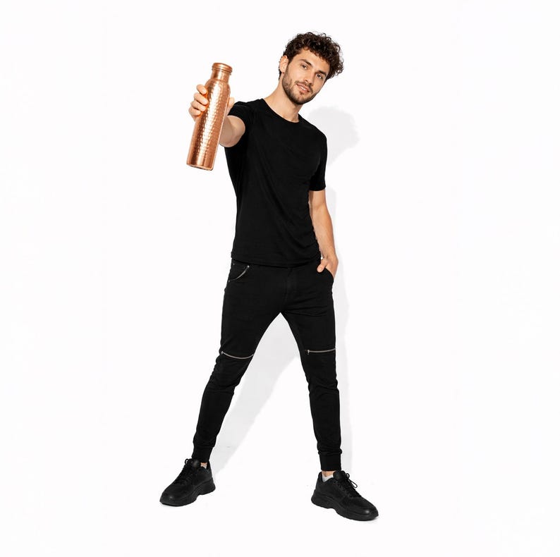 May include: A cylindrical copper water bottle with a textured, hammered surface finish. The bottle features a narrow neck and a matching metallic cap, showcasing a distinct reddish-brown metallic sheen and a reflective, polished appearance.