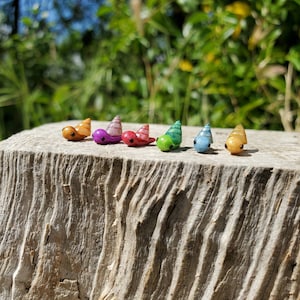May include: Six colorful snail figurines lined up on a wooden surface. The snails are made of a shiny material and have different colors, including purple, green, blue, and orange.