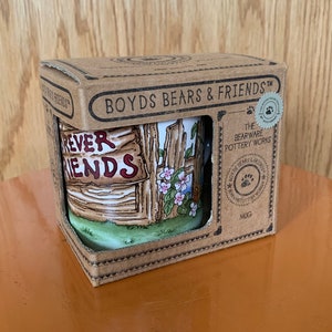 May include: A ceramic mug with the words "Forever Friends" on it, inside a cardboard box. The mug features a painted scene of a wooden fence with flowers. The box is labeled "Boyds Bears & Friends" and "The Bearware Pottery Works".