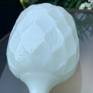 K&ouml;nnte beinhalten: Wei&szlig;e Milchglasvase mit einem strukturierten, geometrischen Design. Die Vase hat einen runden, bauchigen oberen Teil und einen langen, schlanken Stiel.