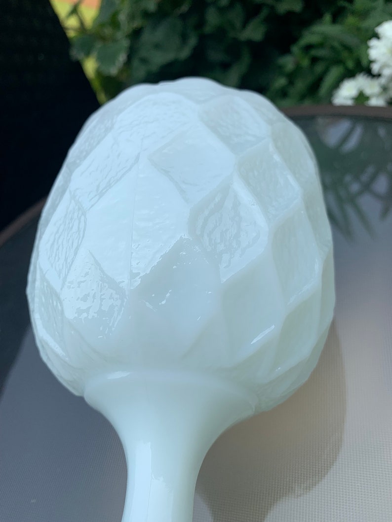 K&ouml;nnte beinhalten: Wei&szlig;e Milchglasvase mit einem strukturierten, geometrischen Design. Die Vase hat einen runden, bauchigen oberen Teil und einen langen, schlanken Stiel.