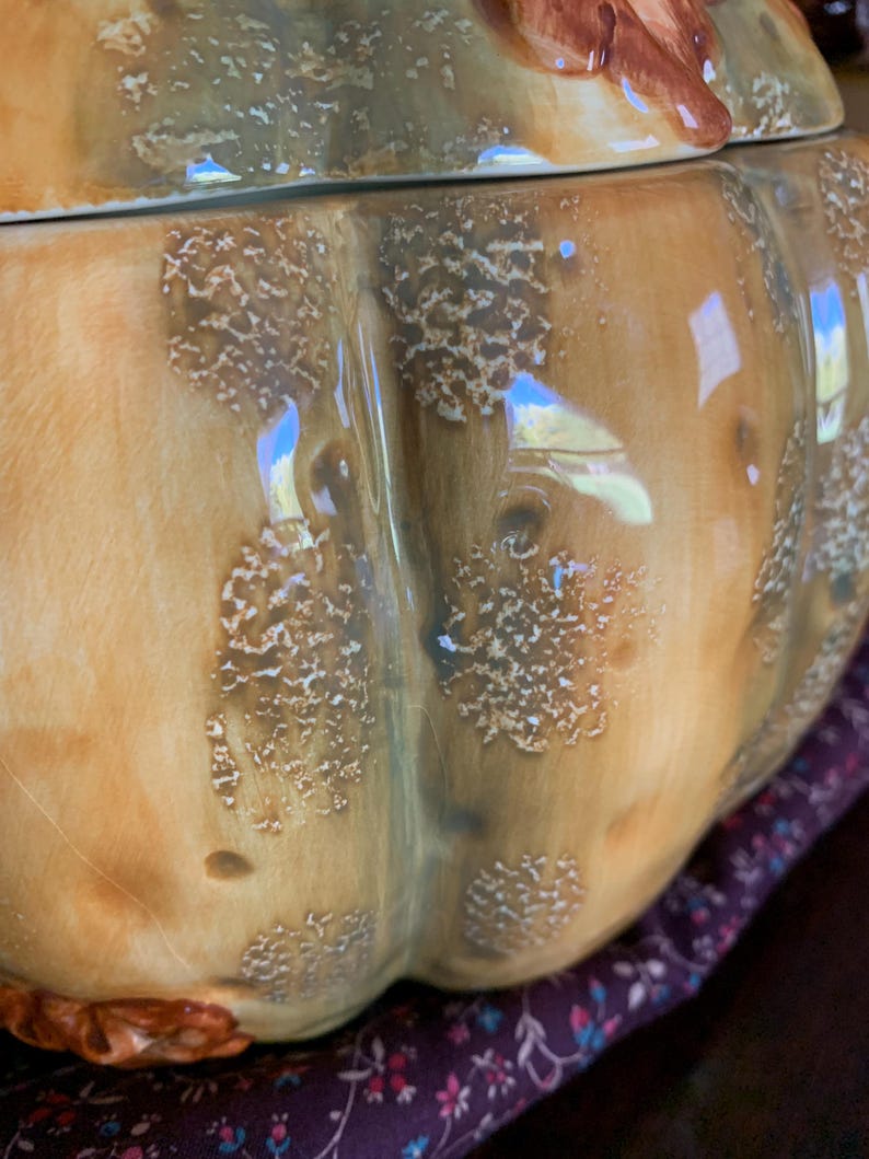 May include: A ceramic pumpkin-shaped cookie jar with a lid. The jar is decorated with a brown and green glaze and has a textured surface. The lid has a small leaf design.