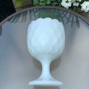 K&ouml;nnte beinhalten: Eine wei&szlig;e Milchglasvase mit einem strukturierten, rautenf&ouml;rmigen Muster. Die Vase hat einen breiten, runden Boden und einen hohen, schlanken Stiel.