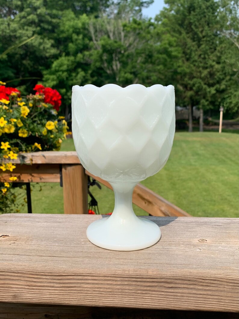 K&ouml;nnte beinhalten: Eine wei&szlig;e Milchglas-Fu&szlig;schale mit einem gewellten Rand und einem Diamantenmuster. Die Schale steht auf einer Holzoberfl&auml;che.