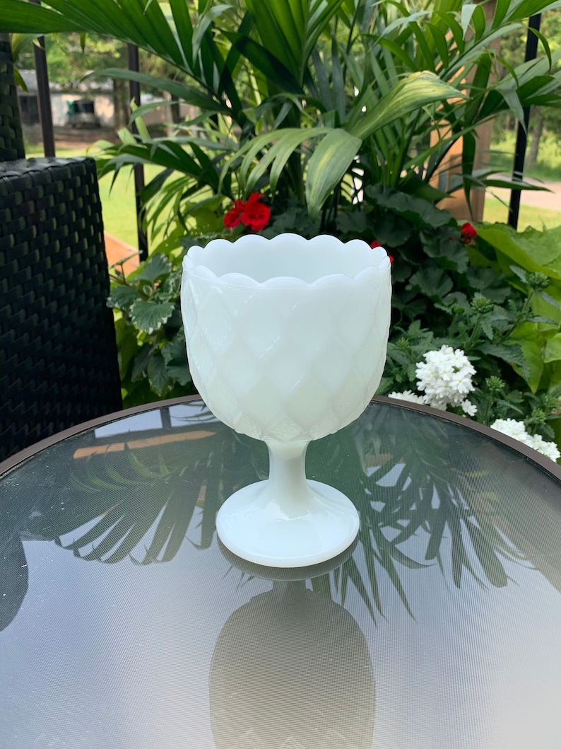 K&ouml;nnte beinhalten: Wei&szlig;e Milchglas-Blumenvase mit gewelltem Rand und Rautenmuster. Die Vase hat einen Sockel.