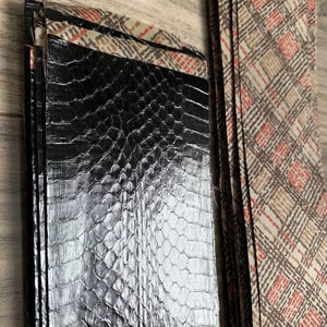 May include: A black leather wallet with a snakeskin pattern and a brown and white plaid fabric lining.