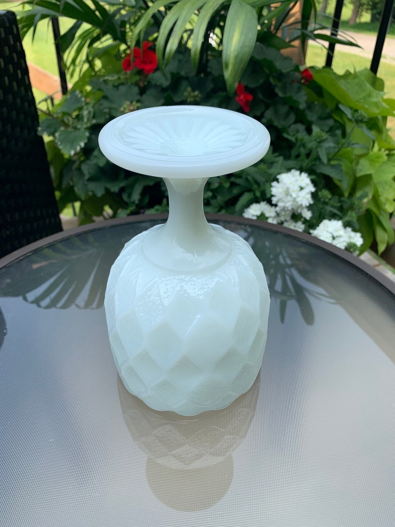 K&ouml;nnte beinhalten: Ein wei&szlig;er Milchglas-Sockel mit einem Diamantenmuster. Der Sockel hat eine breite, flache Oberseite und eine runde Basis.