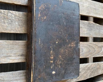 May include: A vintage, black leather-bound book with a worn and aged appearance. The cover is heavily textured and shows signs of use over time.