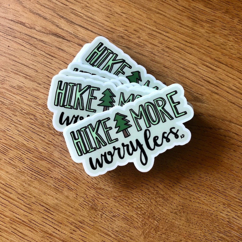 May include: A stack of white stickers with green and black text that reads "Hike More Worry Less" with a small green tree graphic.