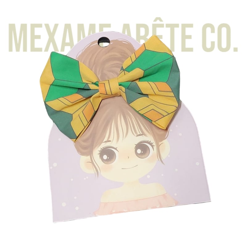 Puede incluir: Un lazo verde y amarillo con un patr&oacute;n geom&eacute;trico. El lazo est&aacute; en una tarjeta con una ilustraci&oacute;n de dibujos animados de una ni&ntilde;a con cabello casta&ntilde;o.