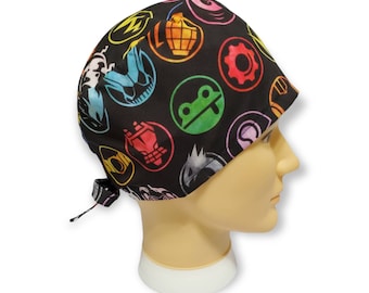 May include: Black scrub hat with colorful circular icons, including a frog, a bomb, and a gear. The hat has a tie at the back.
