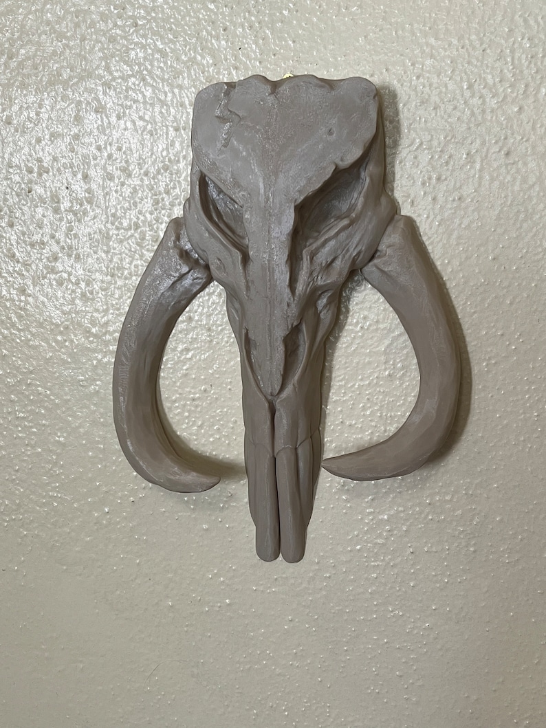 Peut inclure: Un cr&acirc;ne sculpt&eacute; gris avec de grandes cornes incurv&eacute;es. Le cr&acirc;ne pr&eacute;sente des d&eacute;tails et est mont&eacute; sur un mur de couleur claire. La sculpture est une pi&egrave;ce d&eacute;corative, peut-&ecirc;tre pour une pi&egrave;ce ou une collection th&eacute;matique.