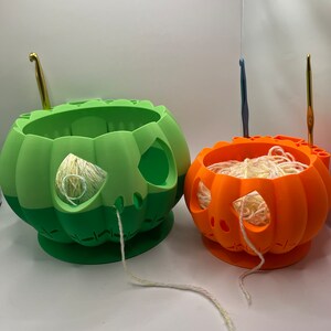 May include: Two pumpkin-shaped yarn bowls, one green and one orange, with yarn and crochet hooks.