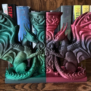 Peut inclure: Une paire de serre-livres en forme de dragon, l'un vert et l'autre rouge, avec des ailes déployées. Les serre-livres sont en matériau imprimé en 3D et sont conçus pour maintenir les livres à la verticale.