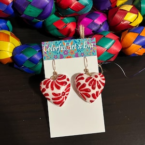 May include: White heart-shaped earrings with red floral designs. The earrings are hanging on a white card with the text "Colorful Art x Eva". Colorful woven spheres in various colors are in the background.