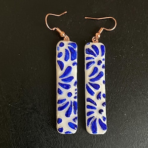May include: A pair of white ceramic earrings with blue floral designs and rose gold hooks.