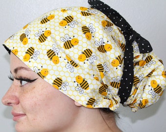 May include: A yellow and black patterned surgical scrub hat with a black and white polka dot tie. The hat features a repeating pattern of cartoon bees on a honeycomb background.