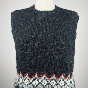 Puede incluir: Un chaleco de punto gris oscuro con cuello redondo. La parte inferior del chaleco presenta un diseño estampado en rojo, blanco y azul. El chaleco se exhibe en un maniquí.