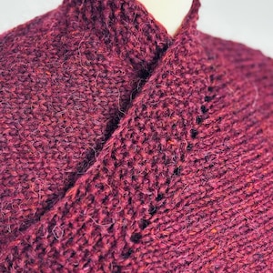 Puede incluir: Primer plano de un suéter de punto burdeos con cuello chal. El suéter está hecho de un hilo suave y peludo y tiene un punto texturizado.